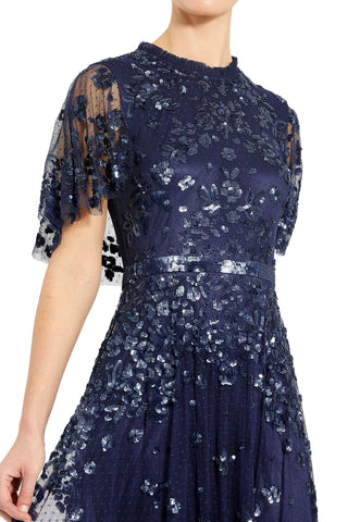Close-up of the ruffled high neckline, flutter sleeve and sequin belt on the navy gown by Mac Duggal at Mrs. G