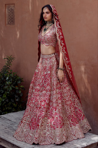 Full-length side view of rosewood red bridal lehenga with dupatta over one shoulder on a stone platform by Osaa by Adarsh at Mrs. G